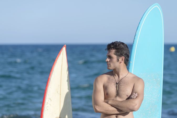 Male surfer standing with boards in front of the ocean