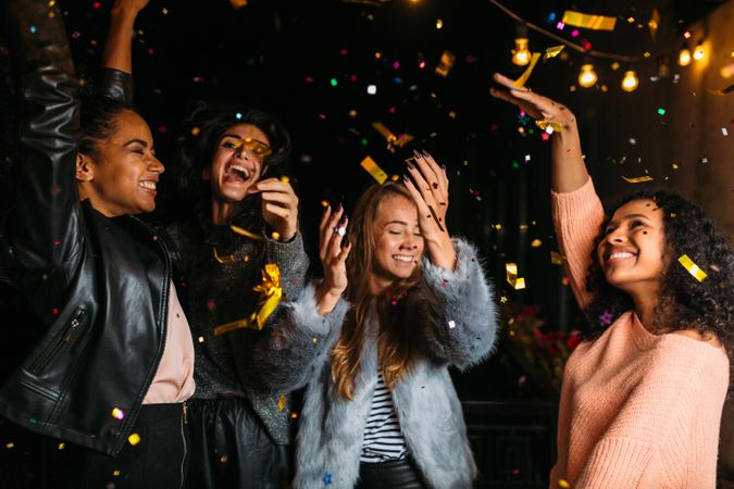 Multi-ethnic group of stylish women throwing confetti at night