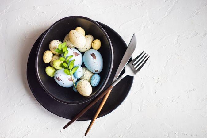 Easter table setting with colorful eggs of difference sizes in dark bowl