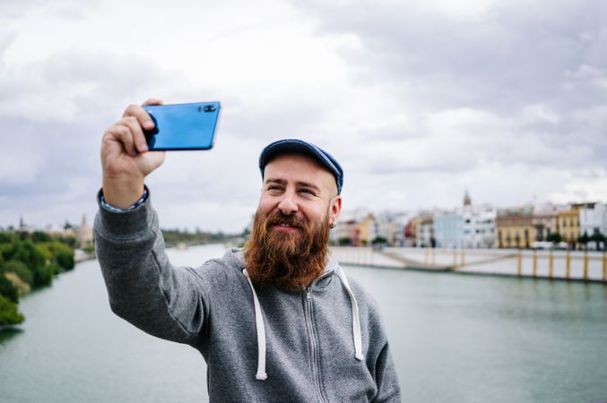 Satisfied male tourist taking selfie on smartphone at quay