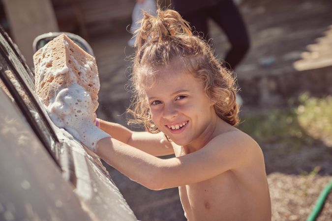 Cheerful boy washing car on sunny day