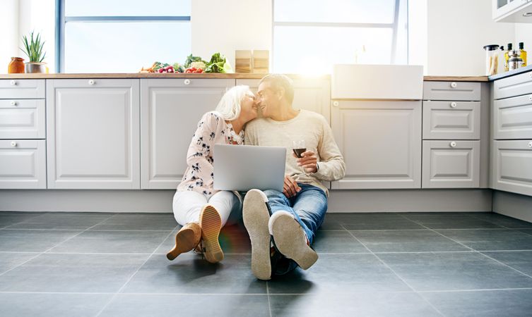Older couple relaxing on kitchen floor with wine and computer