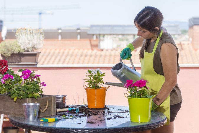 Young woman wearing a gardening apron watering a plant on balcony
