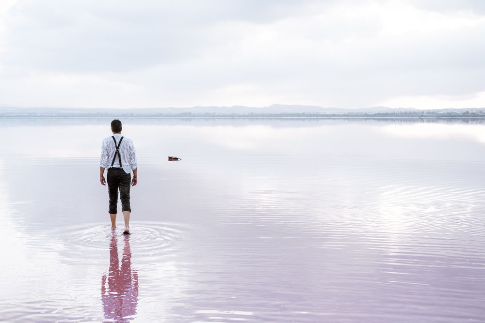 Man in wet shirt picking up guitar floating in water