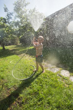 Little child having fun with garden hose and water