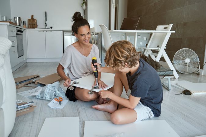 Happy mother and son using screwdriver while assembling furnitur