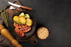 Top view of plate with grilled sausages, potatoes, lime slices and sprig of rosemary with space for text