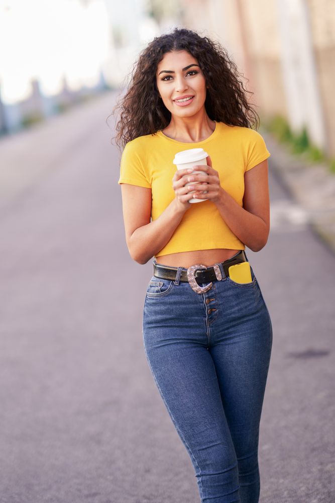 Female in yellow t-shirt walking on street with coffee, vertical composition