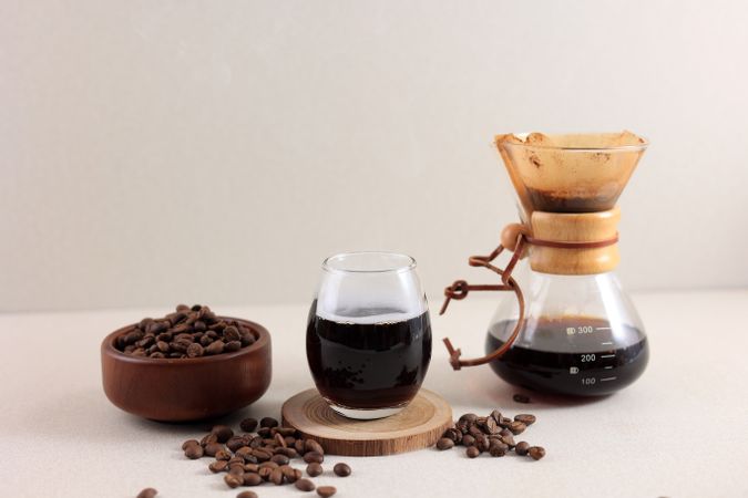 Glass Chemex Coffeemaker with Tasty Drip Coffee and Beans on Cream Table