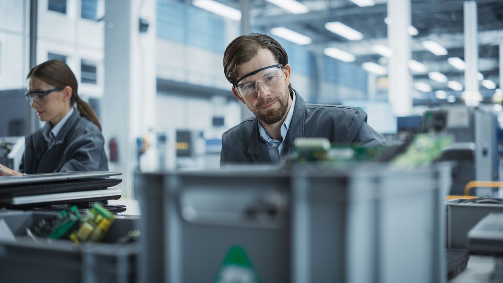 Male And Female Employees Taking Apart Old Laptops To Recycle Components For Sustainable Production Of Electronic Devices At Electronics Factory.