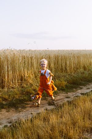 Cute little kid smiling while strolling on path near wheat field