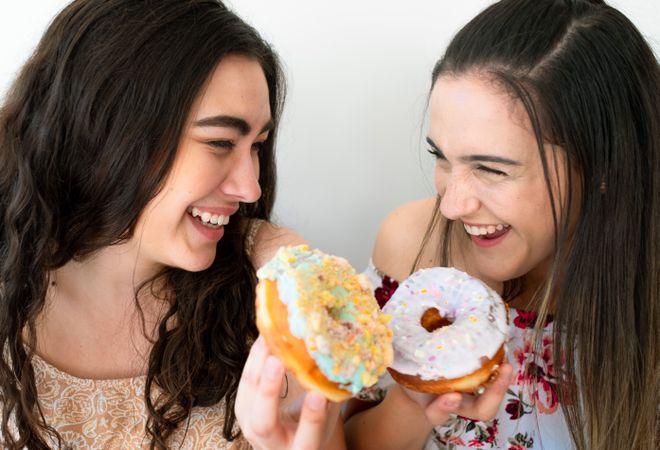 Joyful female friends eating donuts at wall