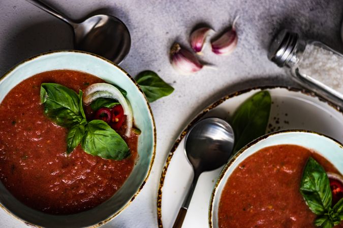 Looking down at two bowls of traditional gazpacho soup with olive oil, basil, garlic and pepper