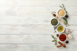 Top view of wooden scoop full of peppercorn with bowls of spice, with copy space