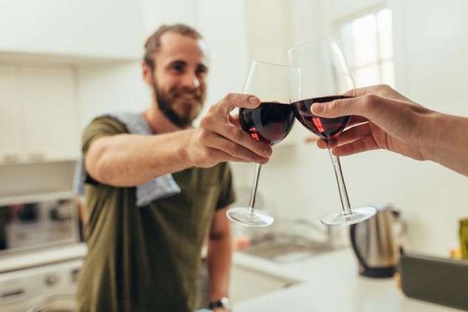 Man standing in kitchen at home toasting wine with a friend