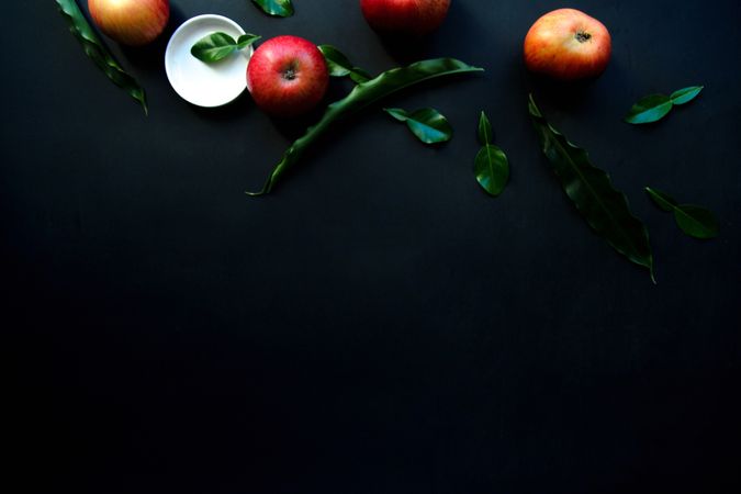 Shiny ripe apples and green leaves on dark background