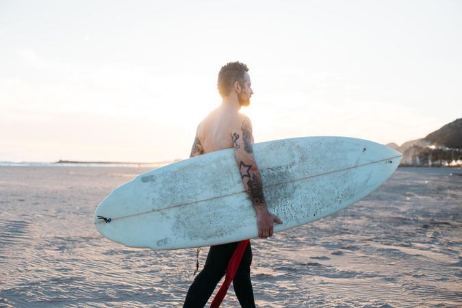 Tattooed man with surfboard under his arm
