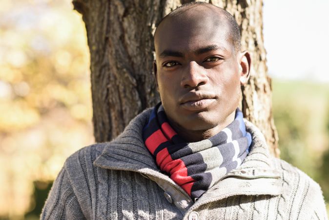 Serious male in sweater standing in front of trees in park