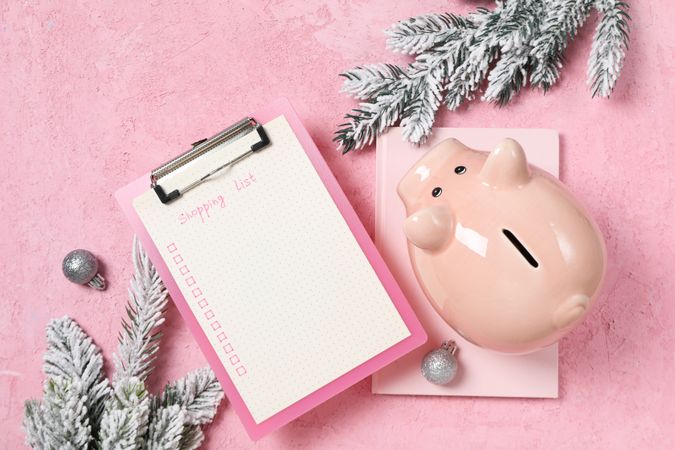 Piggy bank, notepad and folder with list on pink background, top view