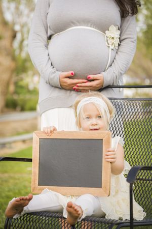 Pregnant Mom Behind Baby Girl in Chair Holding Blank Board