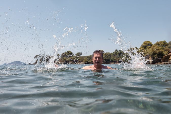 Active older man swimming and splashing in water