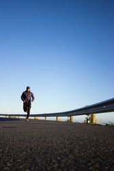 Man in jacket jogging on asphalt road under blue sky bEJz10