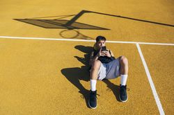 Male basketball player using his smartphone resting after training