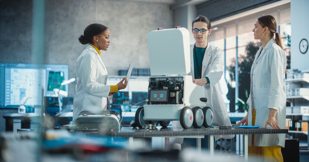 Young Male and Female Engineers in a Lab Discussing an Automated AI Robotic Delivery Assistant