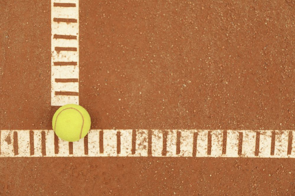 Light green tennis ball on clay court, space for text