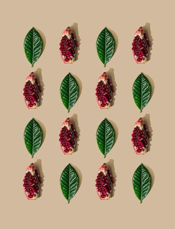 Pattern of green leaves and pomegranate slices on pastel sand background