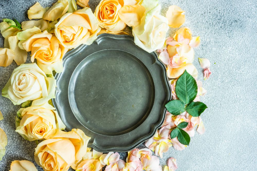 Fresh rose petals surrounding dark plate on counter