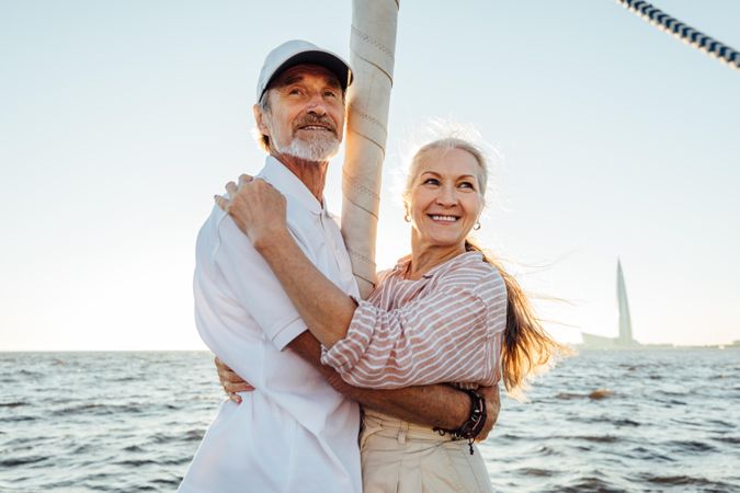 Older man and woman embracing outdoors on boat at sunset