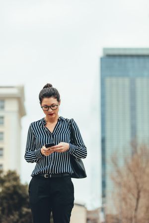 Businesswoman walking outdoors and using cellphone