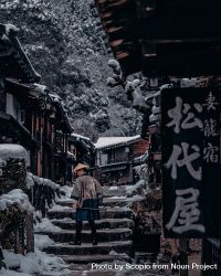 Back view of Japanese person with conical hat walking in snow-covered ancient alley in Japan 48QzRb