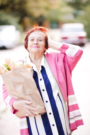 Smiling older woman holding grocery bag standing outdoor