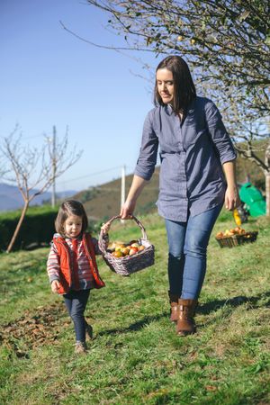 Woman and little girl carrying basket with apples