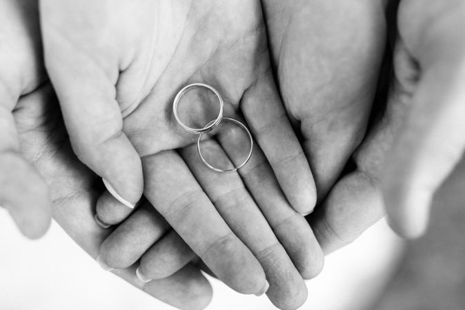 Cropped image of hands holding two wedding rings in grayscale