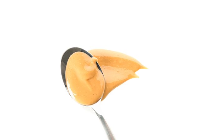 Spoon with creamy peanut butter isolated on light background, top view. A traditional product of American cuisine