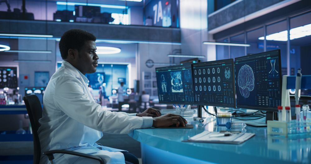 Black Male Neuroscientist Using Desktop Computer To Analyze MRI Scans Of Brain In Medical Research Center Laboratory.