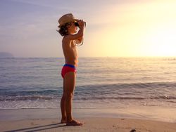 Boy observing sea from binoculars at sunset