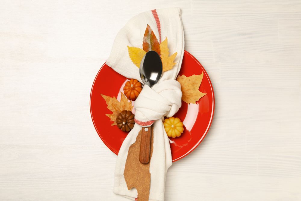 Spoon in towel on plate, leaves and pumpkins on light background, top view