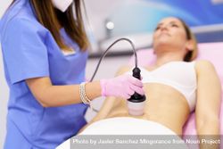 Professional in scrubs performing cosmetic procedure on woman’s stomach bDerp0