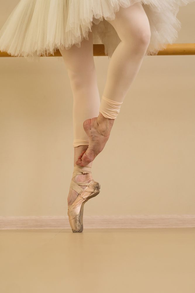 Ballet dancer practicing at barre, one foot in pointe shoes