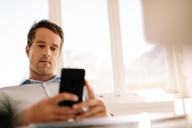 Young male professional using smart phone while working remotely