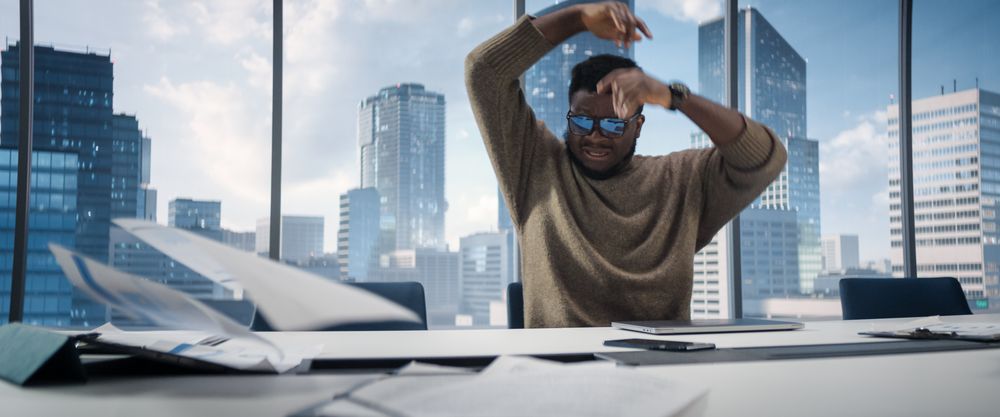 Stressed Out Black Businessman at a Desk in Skyscraper Office, Using Laptop Computer.