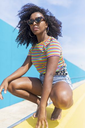 Young Black woman with sunglasses crouched while looking to camera