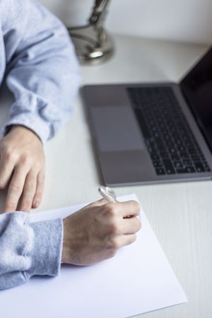 Side view of a young man writing next to laptop at home