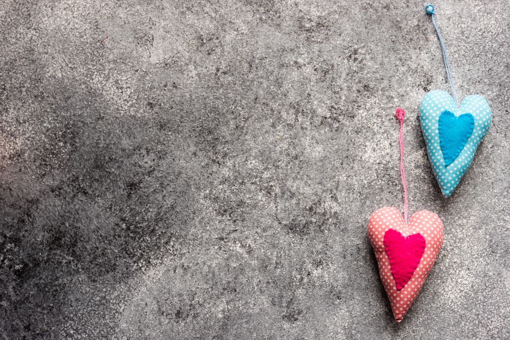 Two blue and pink felt heart ornaments on grey counter