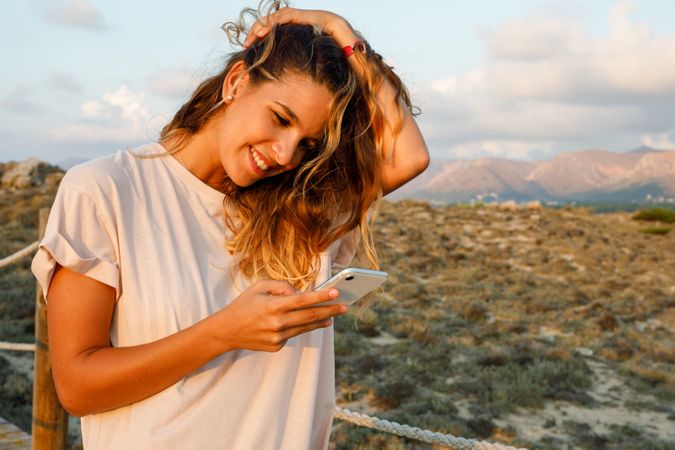 Young hipster browsing smartphone and smiling while walking in nature
