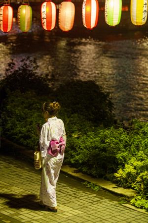 Woman in kimono standing under lit colorful lanterns at night